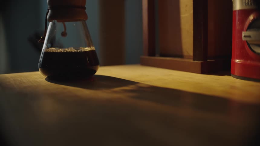Coffee drips into the bottom of a glass container sitting on a wooden surface while coffee is being brewed