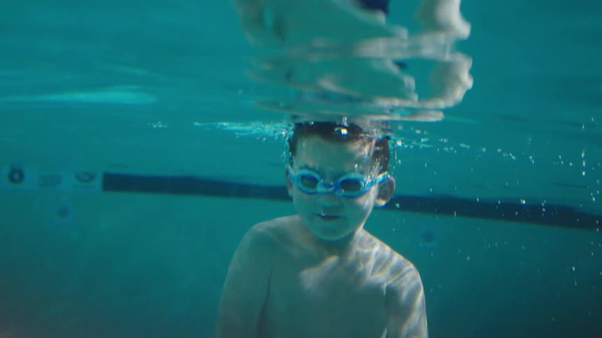 A young boy swims underwater in a clear swimming pool