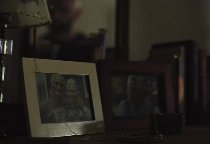 A framed photograph of two older individuals sits on a dark surface with a persons reflection visible in the mirror behind it
