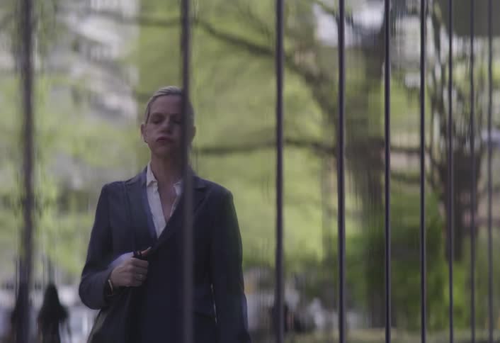 A woman hurriedly checks her reflection in a glass building while rushing to work