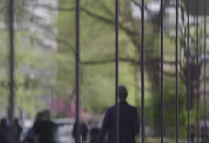 The windows of a building reflect images of the neighborhood and people moving around