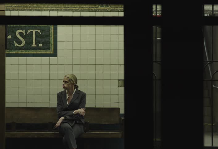 A tired and slightly upset woman sits alone on a subway station bench lost in thought