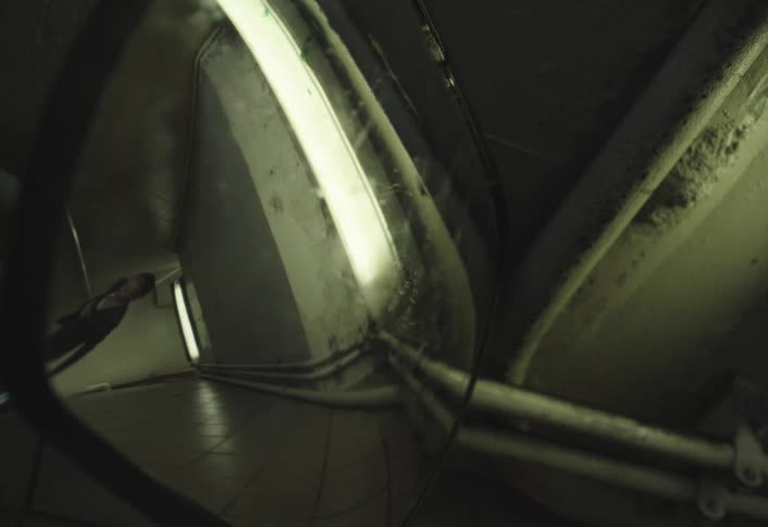 A person is seen in the reflection of a convex mirror in a dimly lit underground corridor