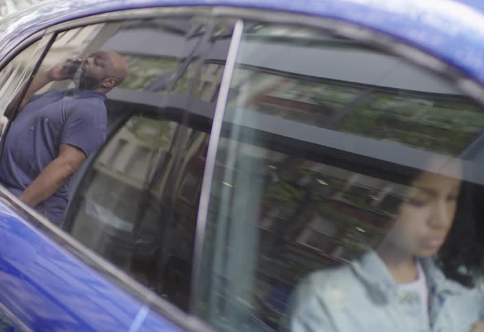 Father closes the car door and stands talking on a smartphone while his daughter waits in the car