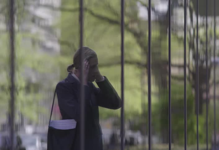 Female pedestrian wearing a suit stops to check her appearance in the reflective surface of a building during the daytime