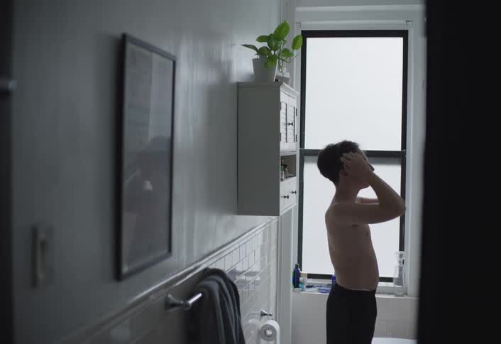 A teenage boy stands in the bathroom wearing only shorts scrubbing and styling his hair