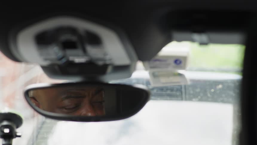 A mans eyes are seen in a rearview mirror while driving in traffic