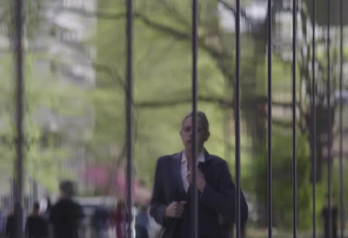 A worried woman in formal wear rushes past a glass wall looking tense and late