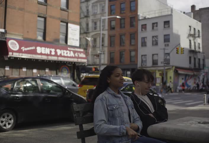 Two people share earphones with a phone reflecting a face on a checkered table