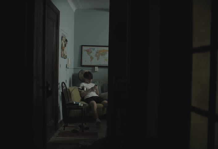 Woman working on a laptop in the living room of the house and in a room a boy sitting using a smartphone