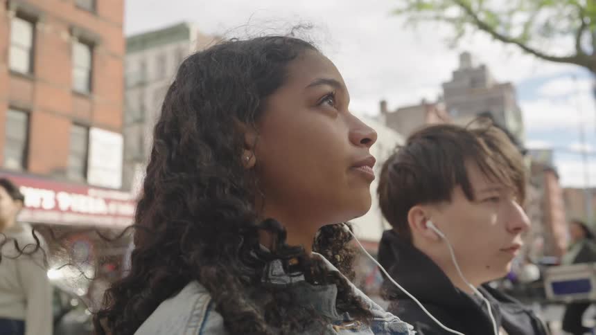 Two people sit outdoors sharing earphones and enjoying music together
