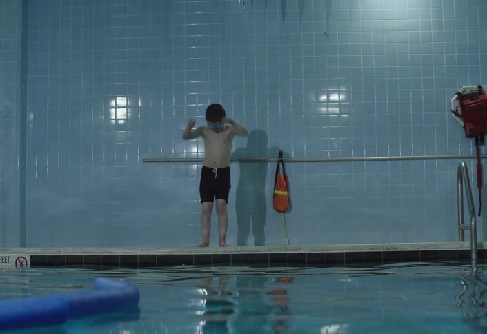 A young boy wearing goggles prepares to swim in an indoor pool