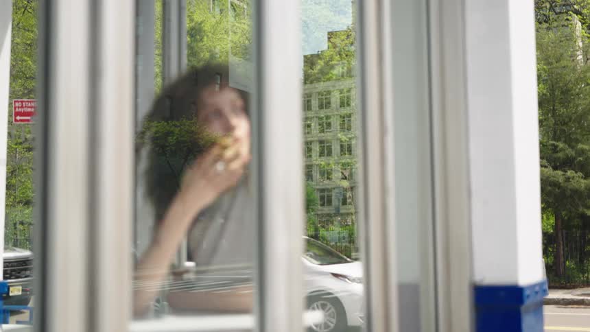 A person is seen through a reflective glass wall seemingly lost in thought