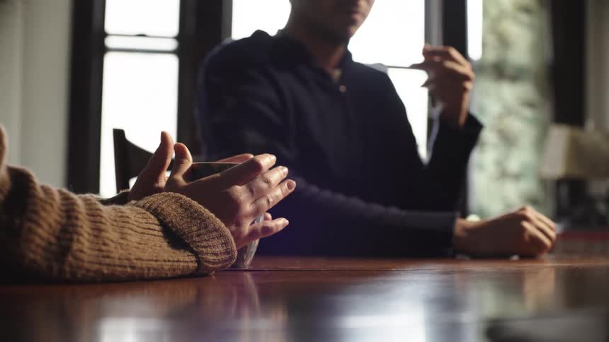 A woman holds a mug of coffee while talking at the table