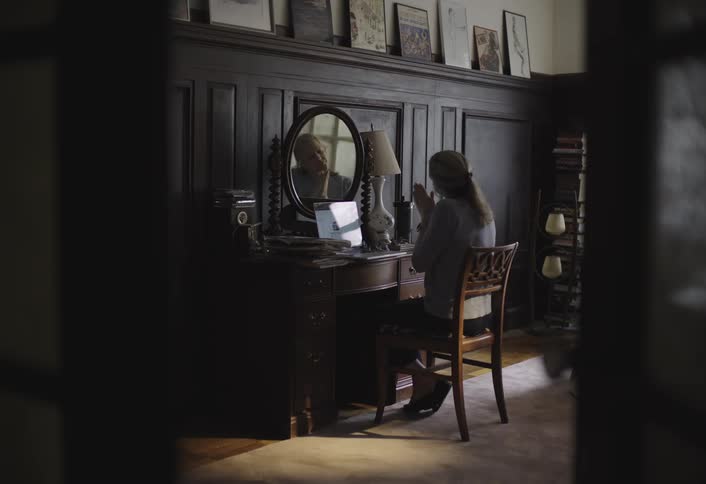 Woman taking off and putting on her glasses while sitting at a desk typing on a laptop