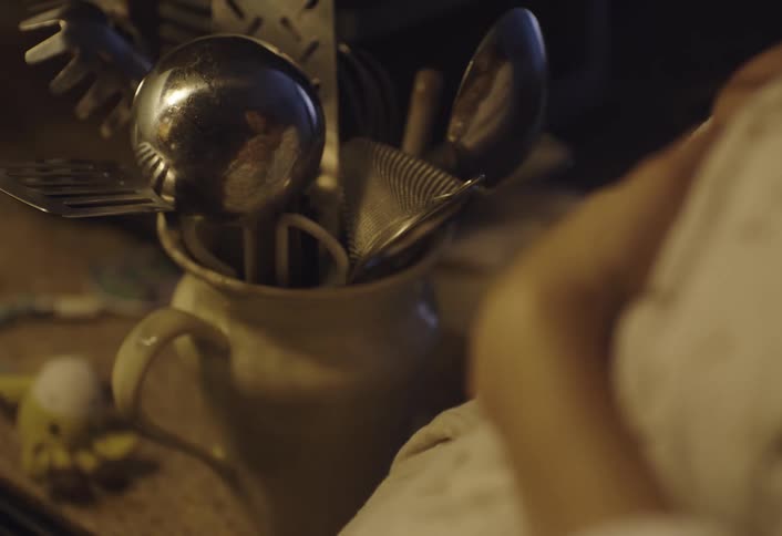 A pregnant woman reflected on a collection of various metal kitchen utensils stored in a white pitcher