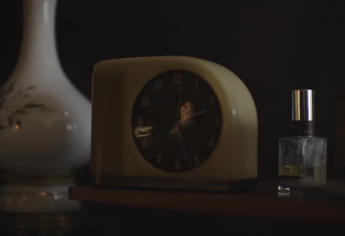 A vintage clock sits on a wooden shelf in dim lighting