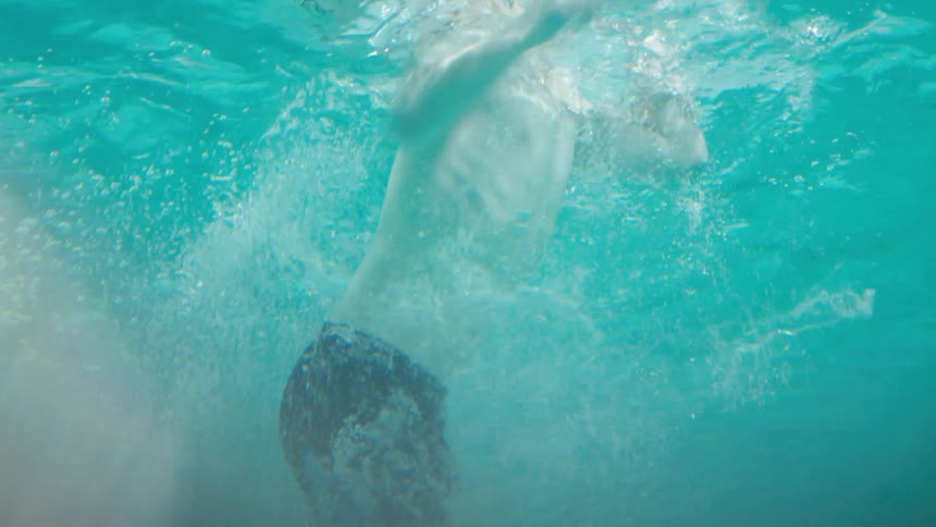 A boy jumps in a pool and swims up to a pool noodle at the surface