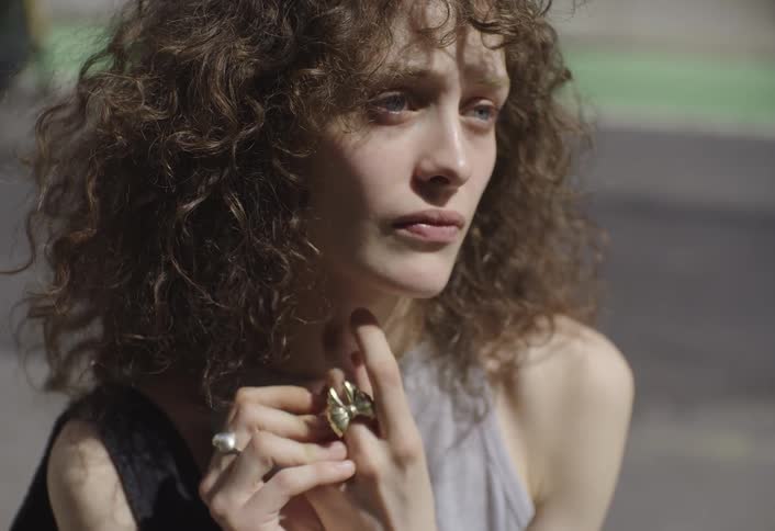 Woman in an outdoor environment with curly hair looking thoughtful