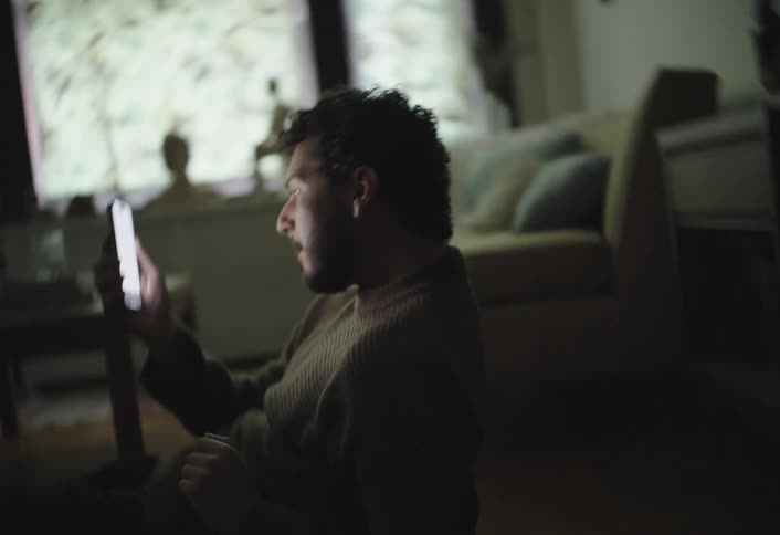 Man lies on the floor in a dim room staring at his phone