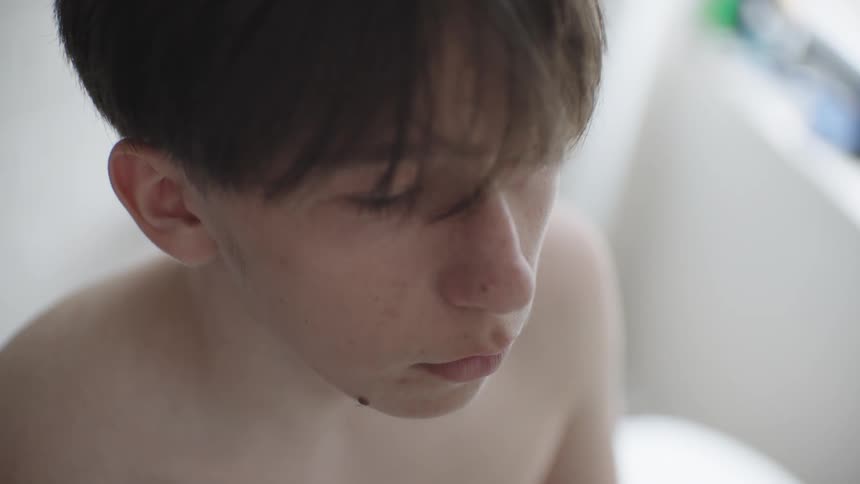 A teenage boy stands inside a bathroom looking sad