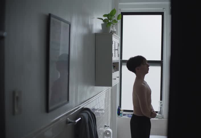 Teen boy stands shirtless in bathroom admiring his muscles in the mirror