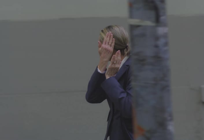 A woman with her hair pulled back wearing a dark suit jacket over a white top walks on a city street