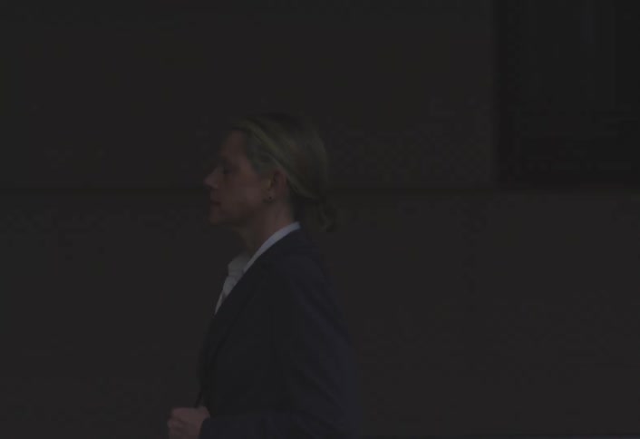 Woman in a charcoal gray blazer and tiedup hair walks hurriedly on a city sidewalk