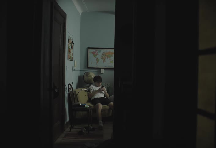 A teenage boy sits in an armchair at midday operating a mobile device