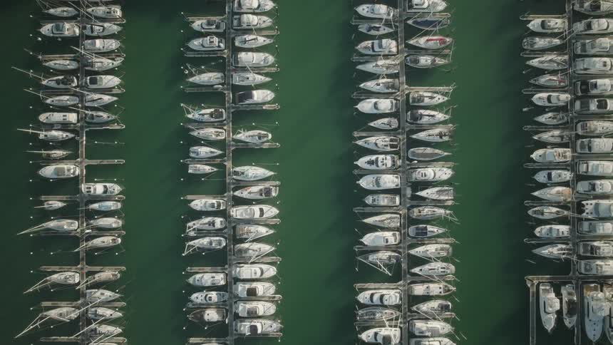 An aerial view captures numerous white boats docked in rows within a marinas green water
