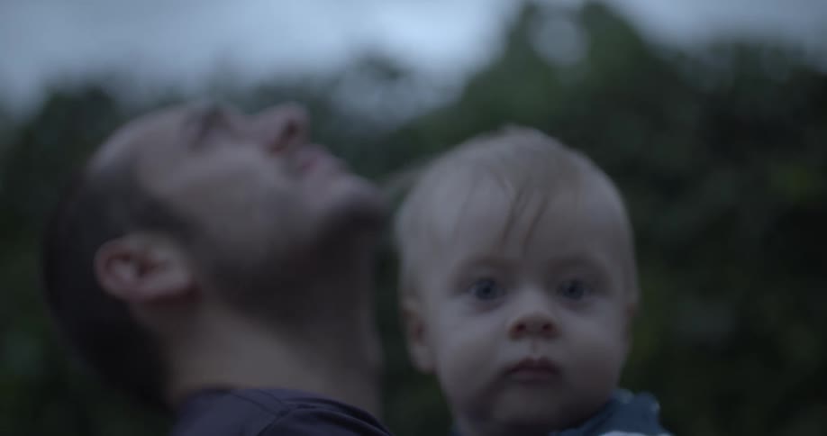 A man holding a baby in his arms looking up at the sky