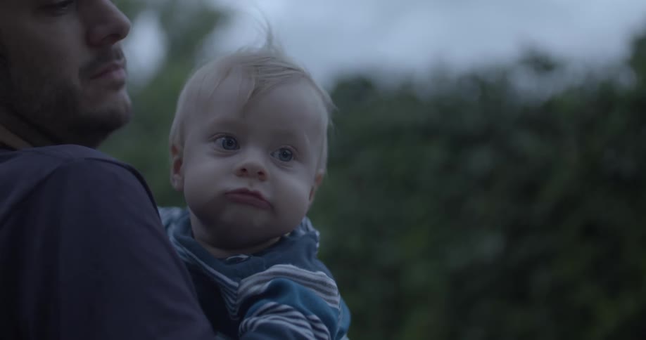 A man holding a baby in his arms gently caressing the babys head with his hand