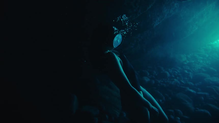 Female free diver in an underwater cave slowly resurfaces