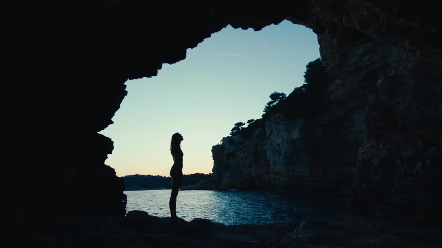 A woman stands in the shade of the cave on the shore