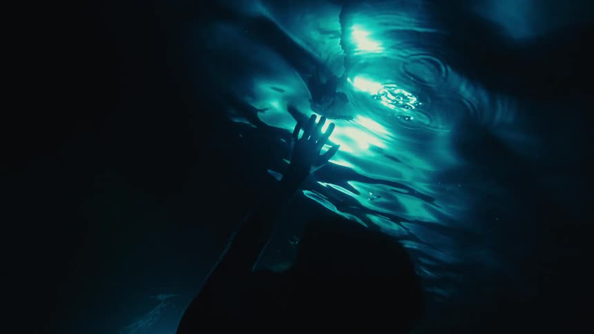 A woman reaches up in the underwater cave
