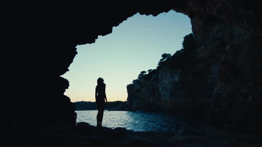 Silhouette of a woman walking on rocks in a seaside cave