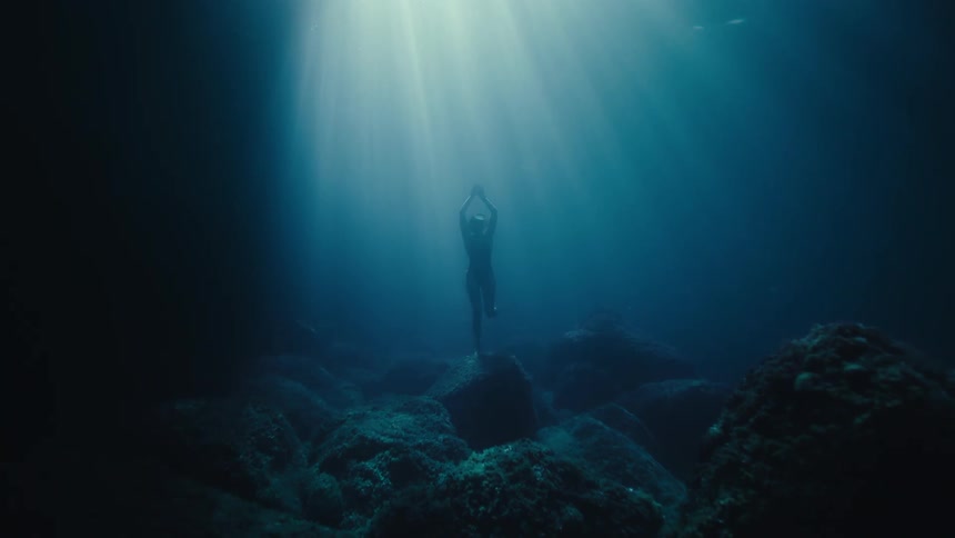 A woman begins swimming up from the ocean floor