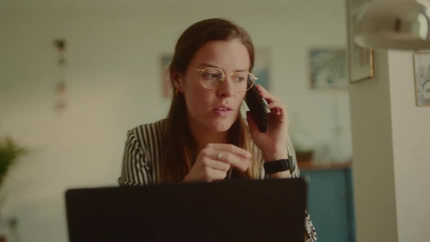 Woman talking on the phone while sitting at a table in front of an open laptop