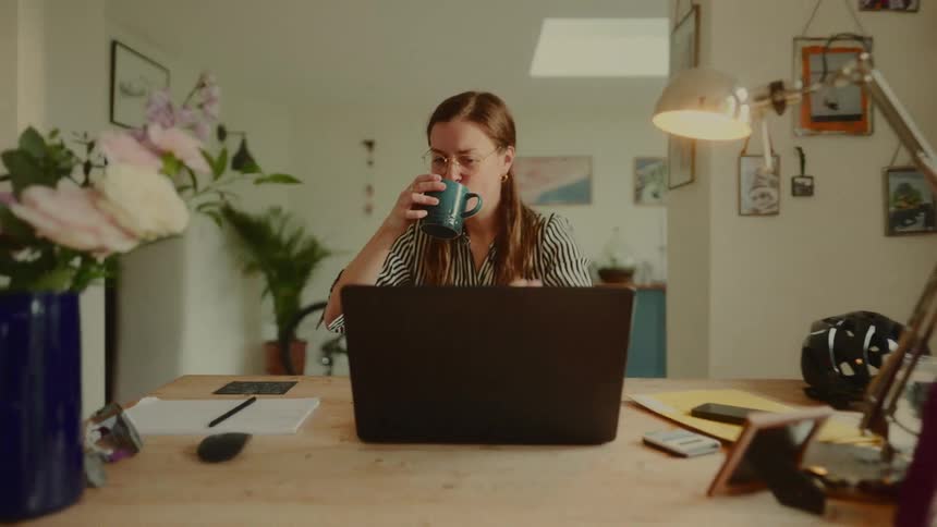 Woman sitting sipping from a mug and opening a laptop