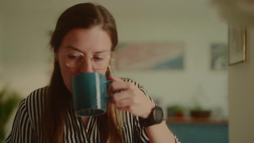 A woman drinks coffee while looking at her laptop