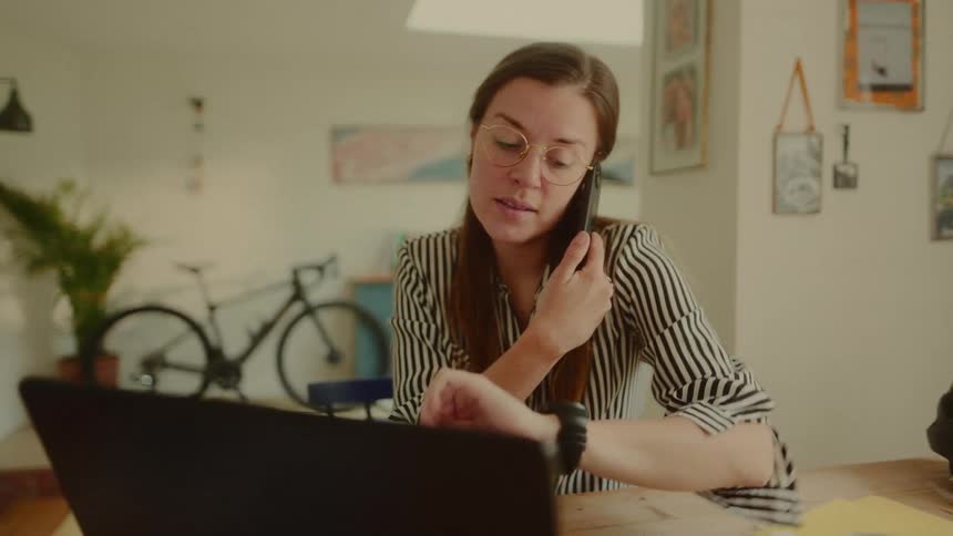 Woman sitting at a desk looking at her watch and talking on a call on her smartphone at the same time