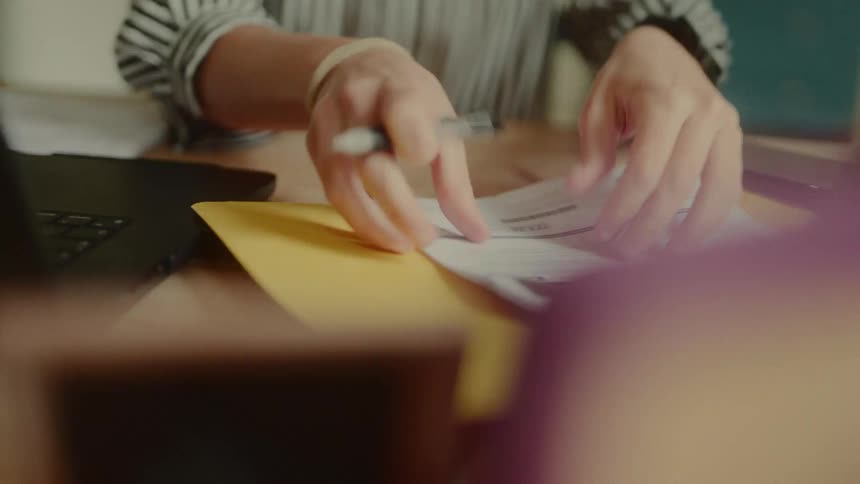 A woman arranges files on a desk while holding a pen