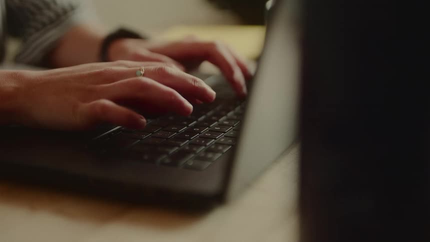 Woman sitting at a table types on a laptop