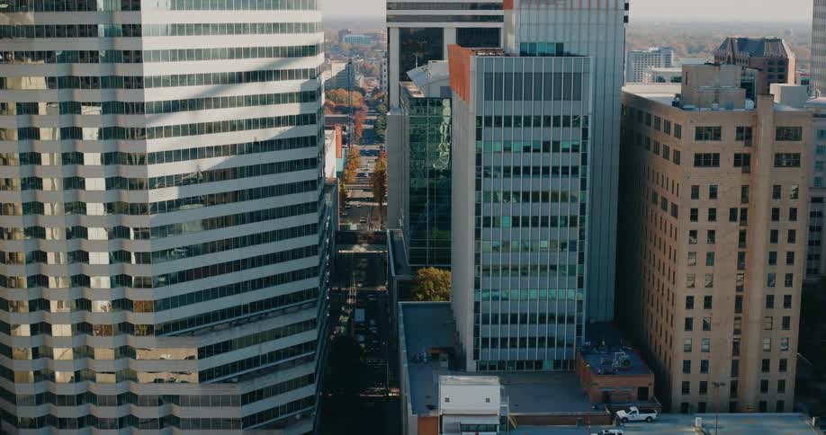 An aerial view captures the dense urban landscape of a city dominated by tall buildings with varied architectural styles and a street winding through them