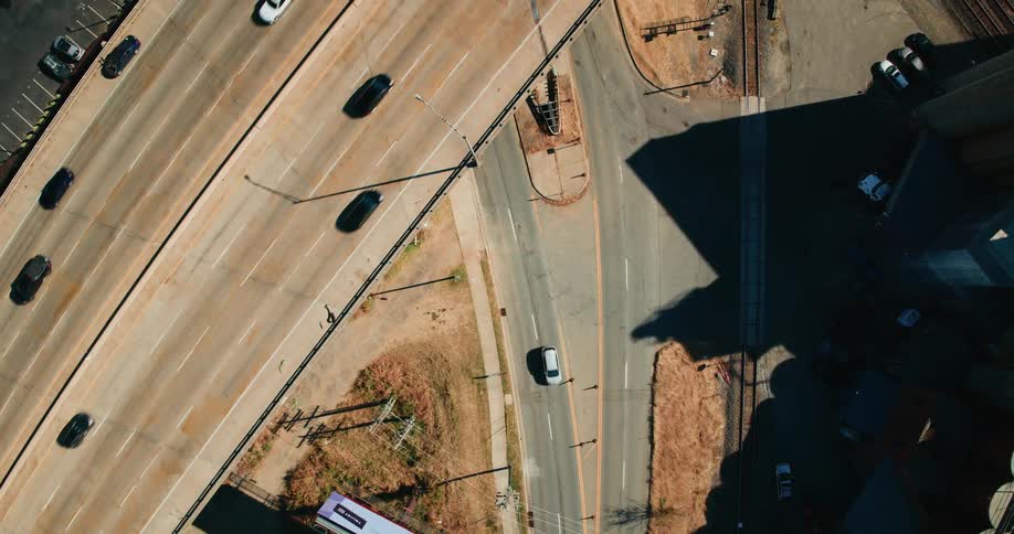 A series of cars pass along the highway near an intersection on a sunny day in the city