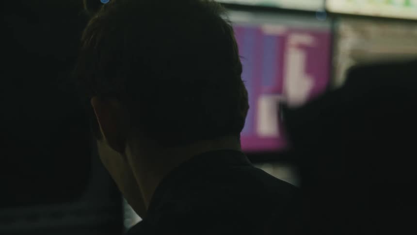 The back of a mans neck with short hair and in front of him there are some screens attached to the wall