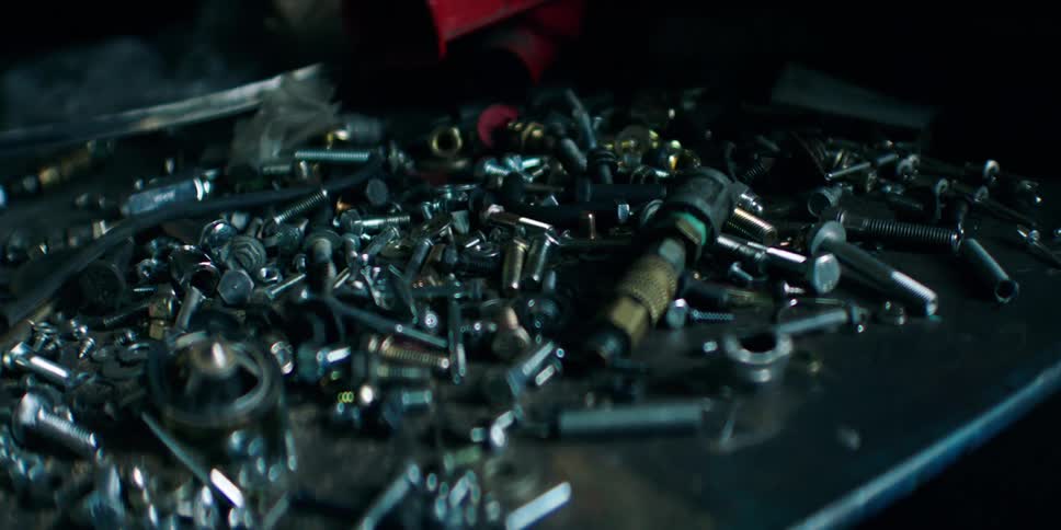 A cluttered metal surface is covered with assorted screws bolts and small hardware parts