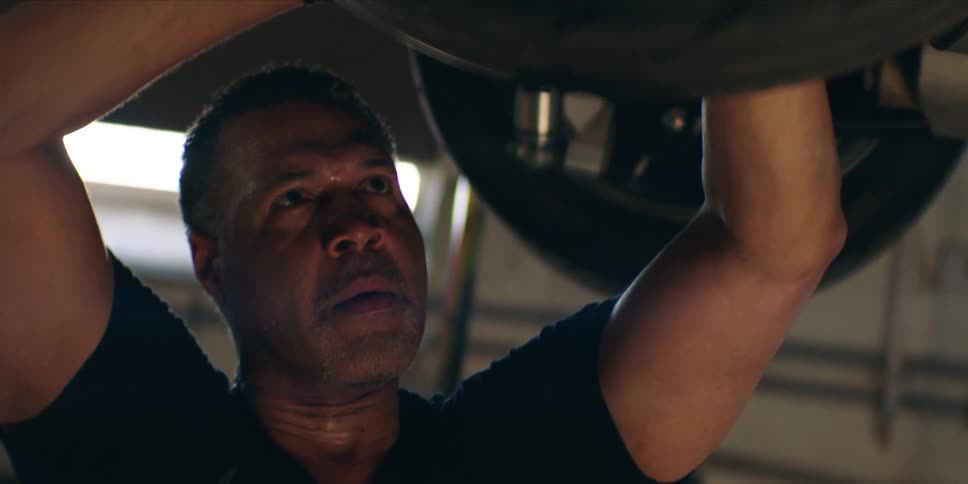 A mechanic works underneath a car inside a mechanic workshop at midday