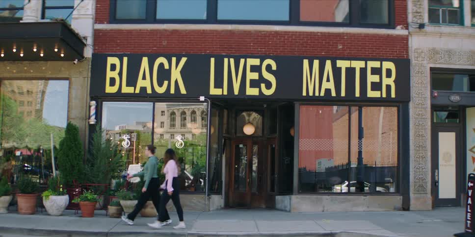 Two people walk past a storefront with a bold black lives matter sign in large yellow letters