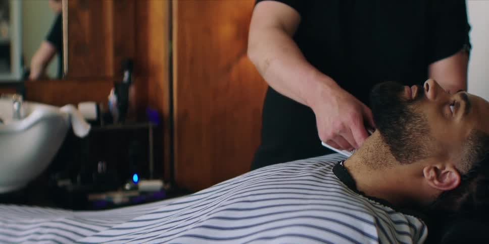 A barber is using clippers to trim a mans beard